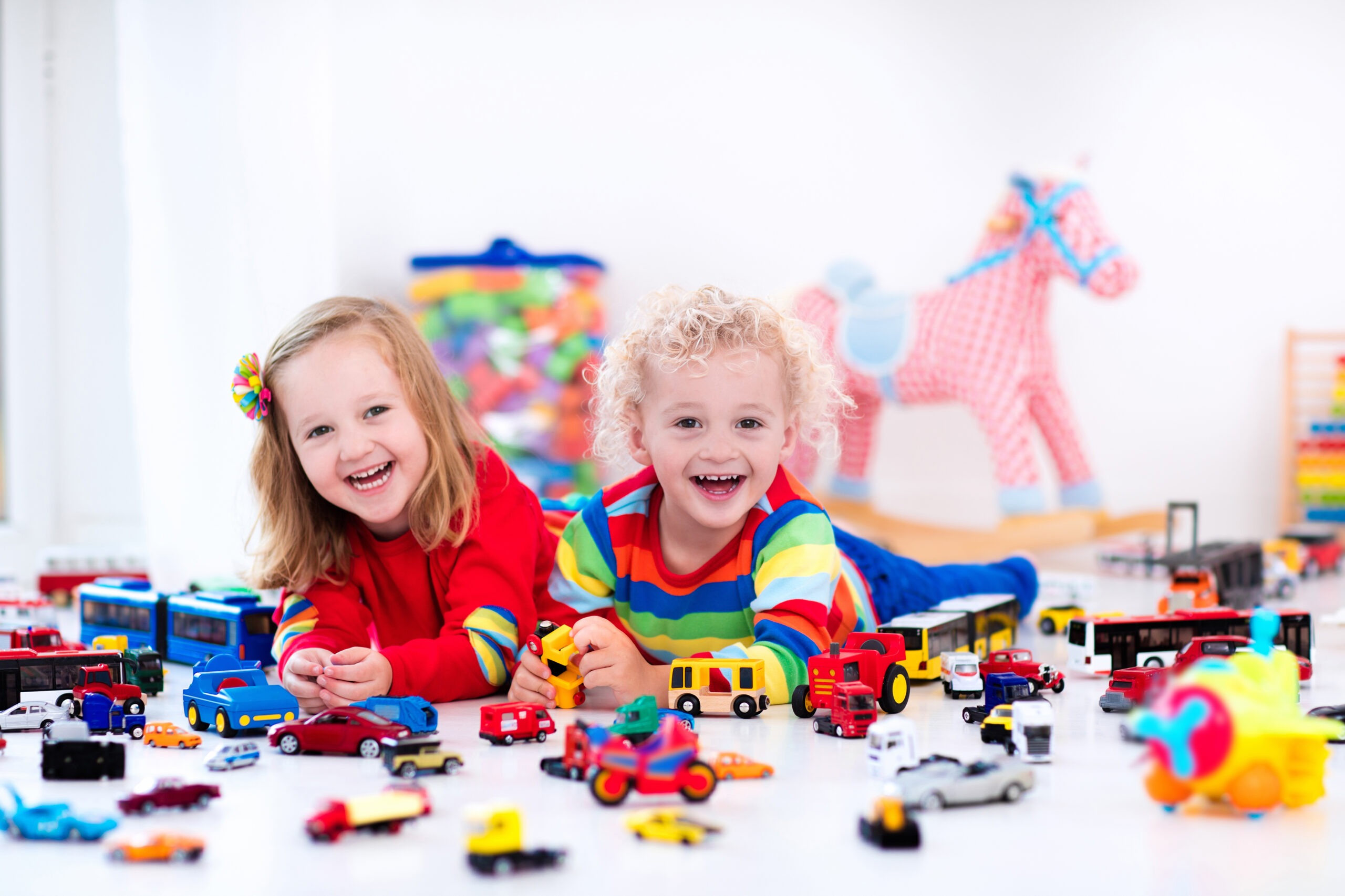 Little toddler boy and girl playing with model car collection on the floor.
