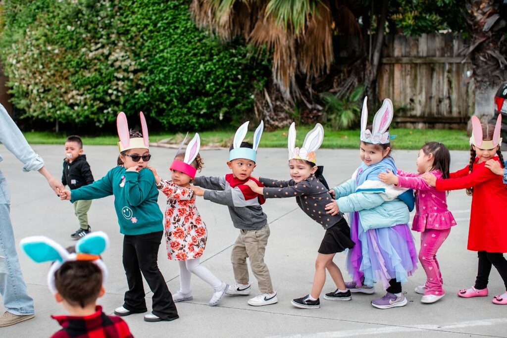 Children in colorful bunny costumes hold hands, smiling joyfully in a playful outdoor setting.