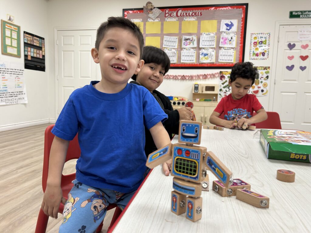 Three young boys joyfully play together with a colorful robot toy on the floor.