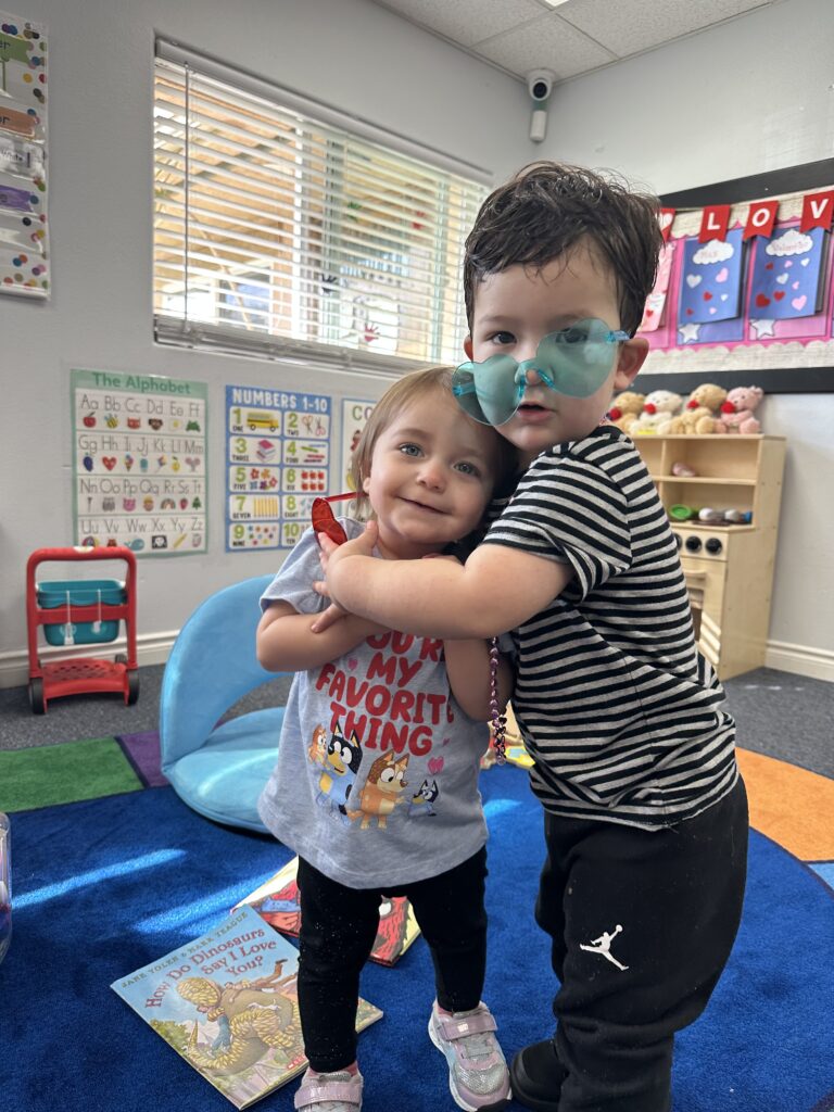 Two masked children in blue are seated in a classroom, participating in a lesson and interacting with their surroundings.