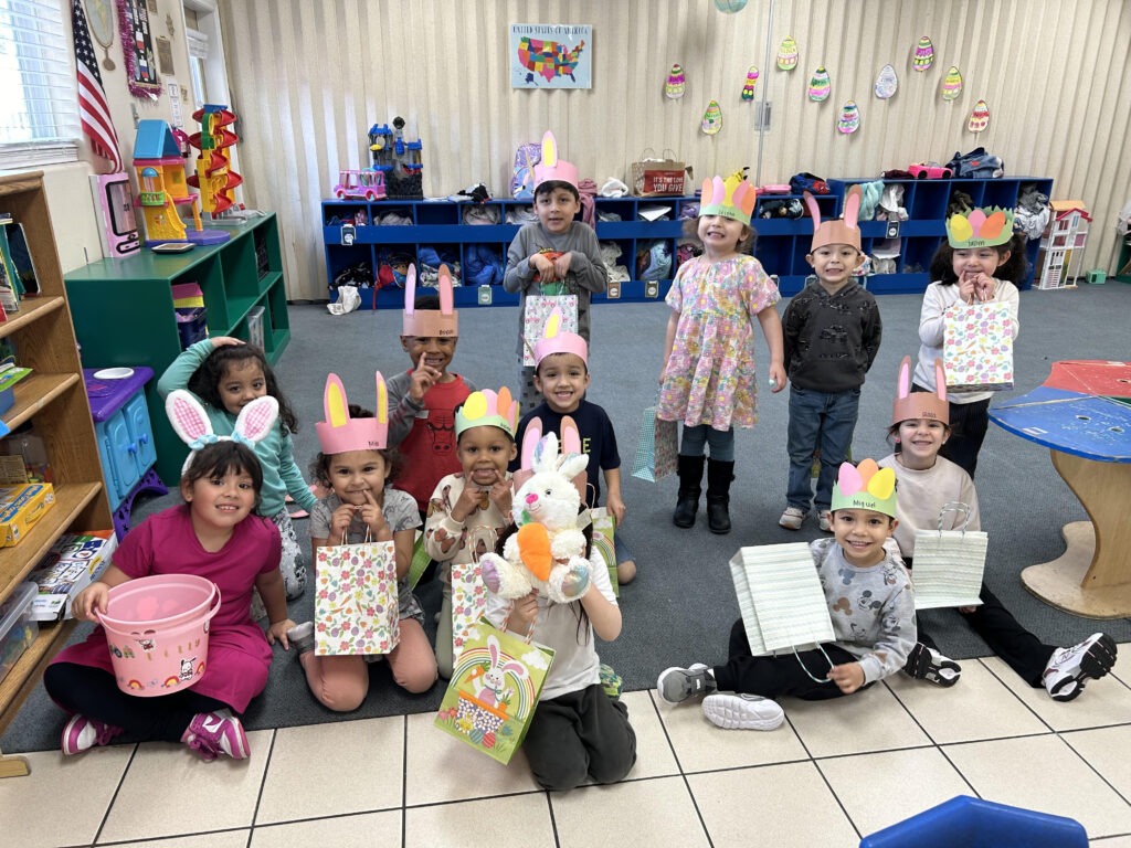 A group of children in bunny hats joyfully holding Easter baskets, ready for an egg hunt in a sunny outdoor setting.